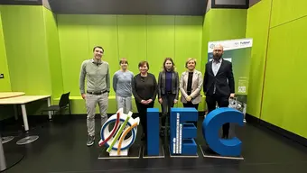 Photo showing six participants from AGH and TU Freiberg during a meeting, standing in front of the IEC lettering.